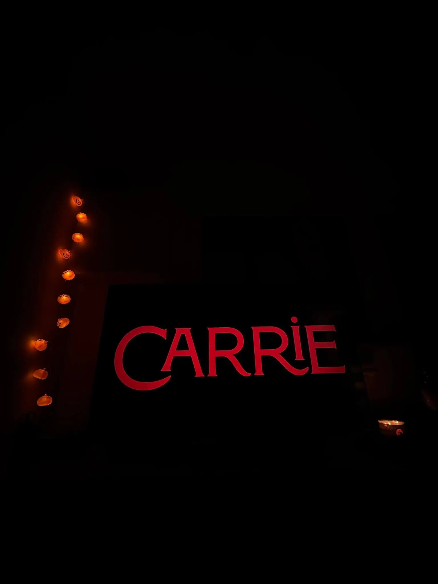 Carrie title card on screen, pumpkin lights glowing beside it